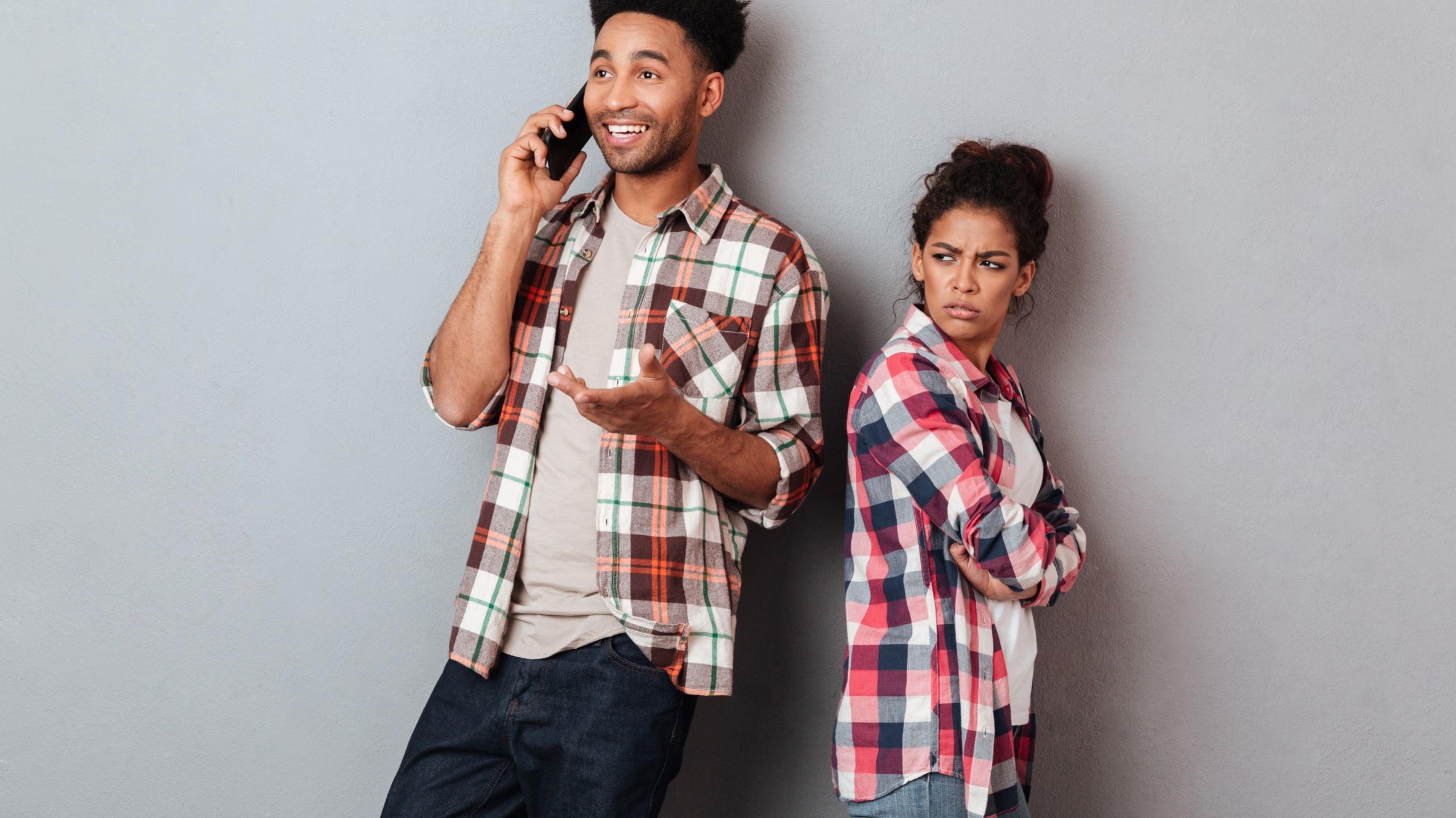 A man laughing and talking on his phone while his girlfriend looks angrily at him.