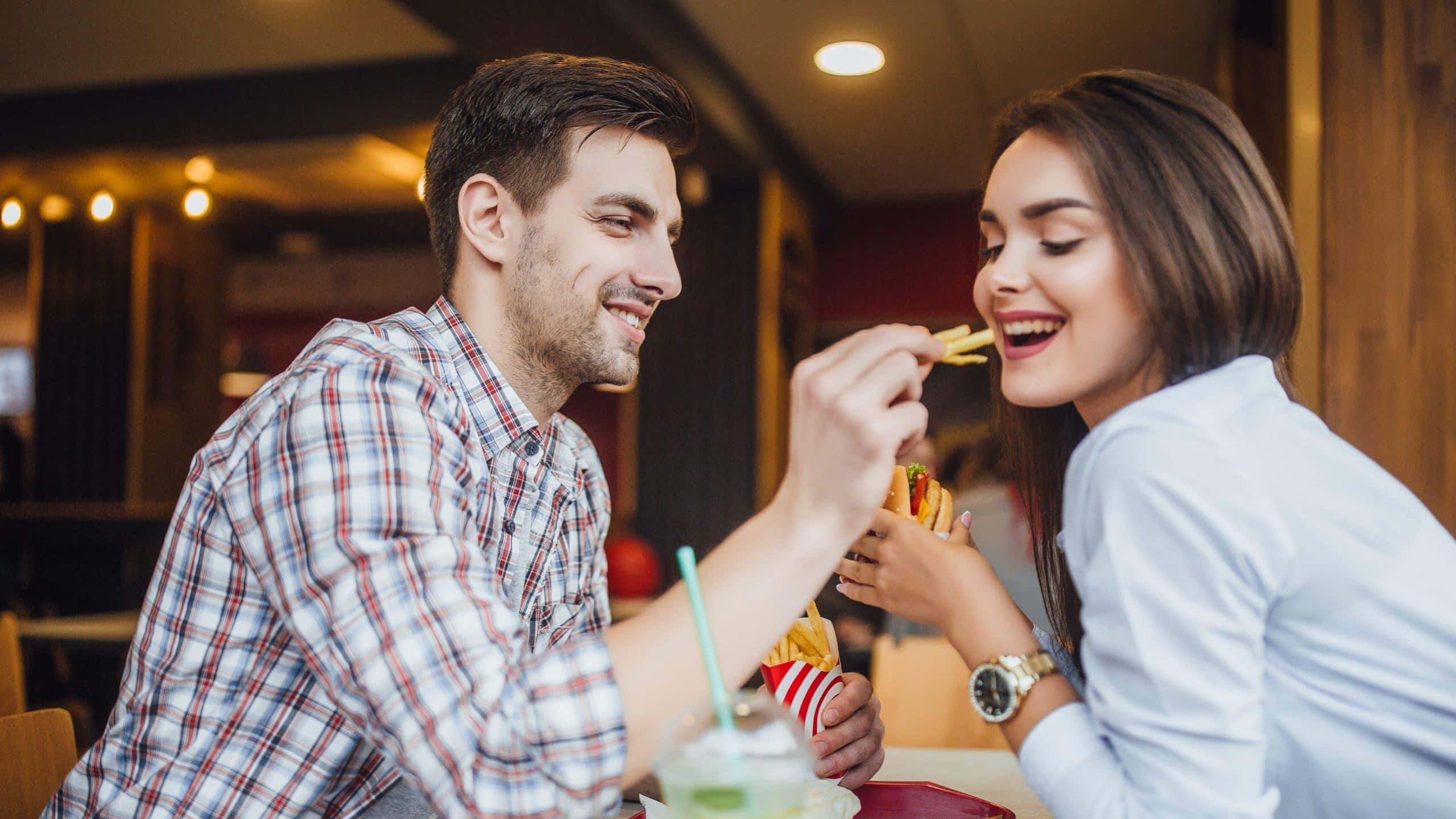 A man feeding fries to his girlfriend at a restaurant.