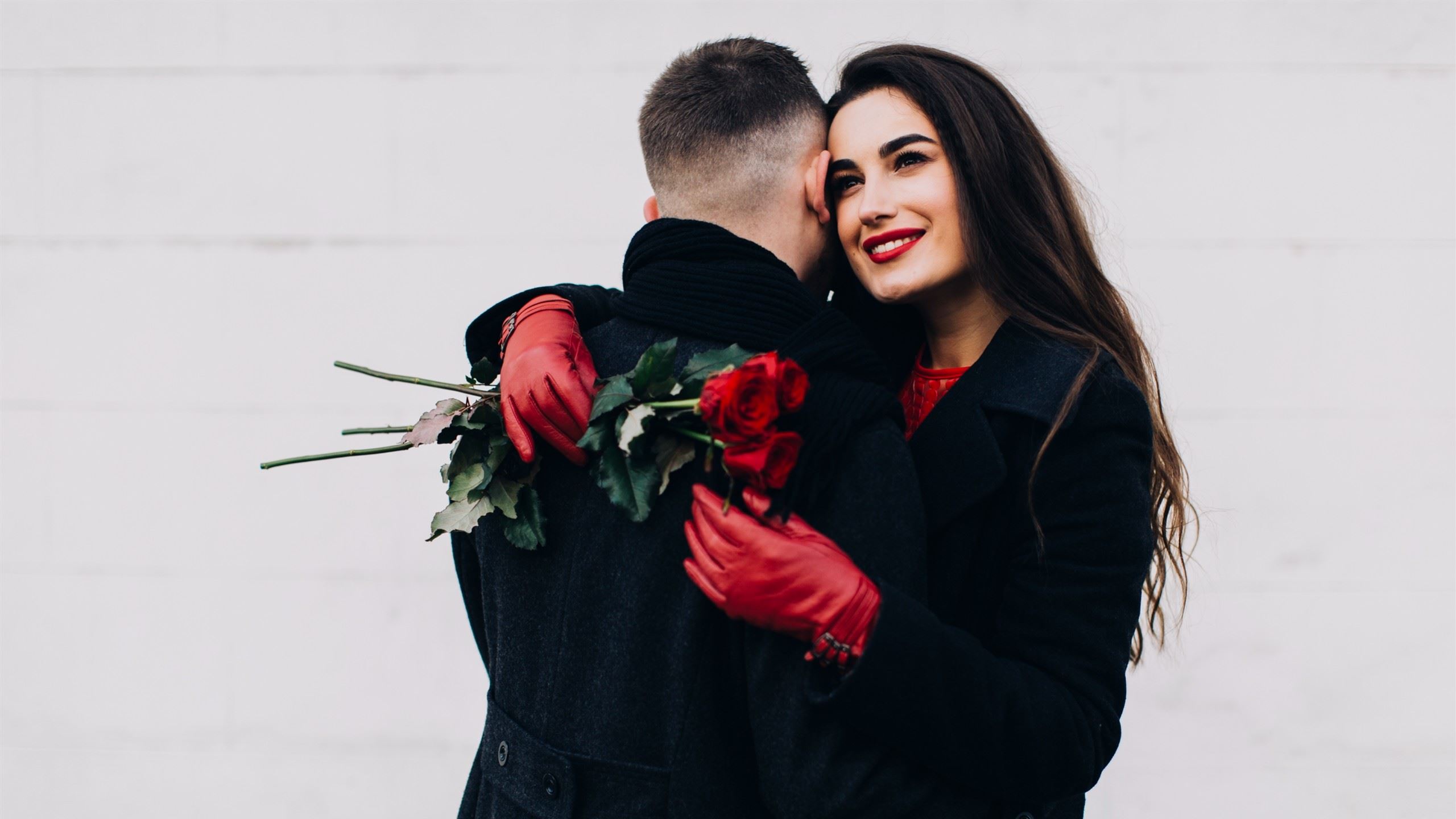 A man hugging a dark-haired woman while she holds roses.