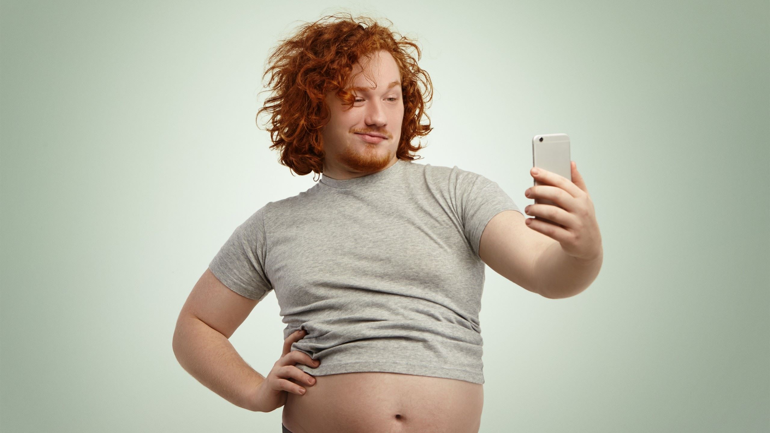 An overweight red-haired man taking confidently a selfie.