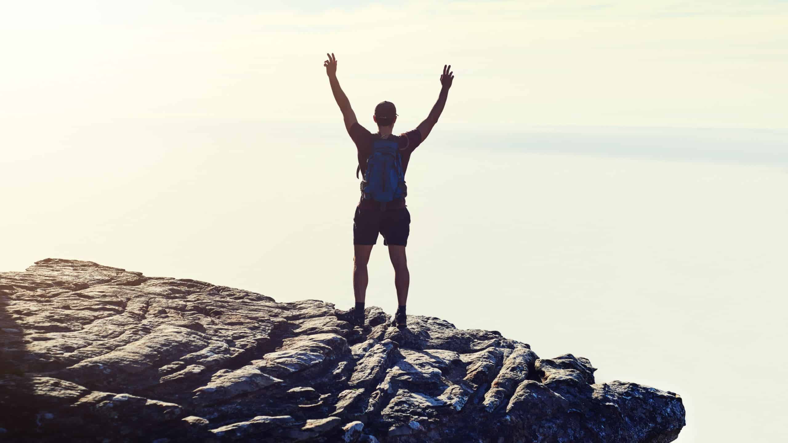 A man standing in a victory pose on a rock.