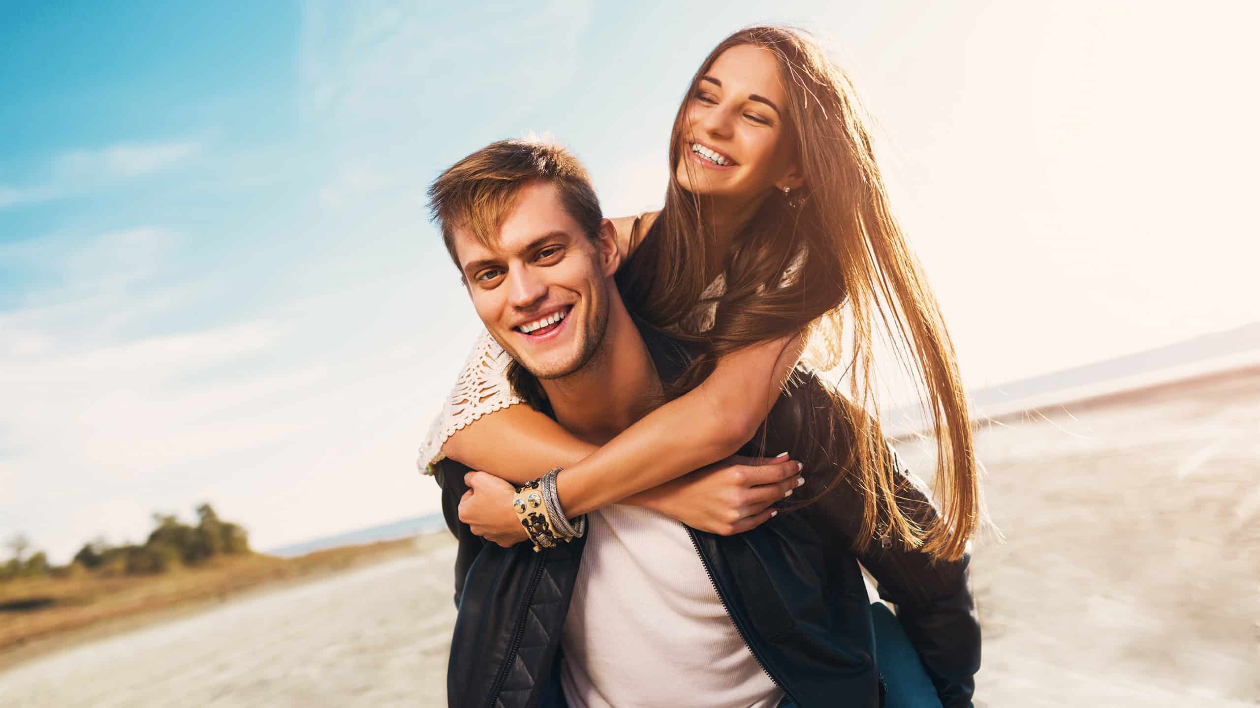 A guy in a leather jacket giving a piggyback ride to his girlfriend.