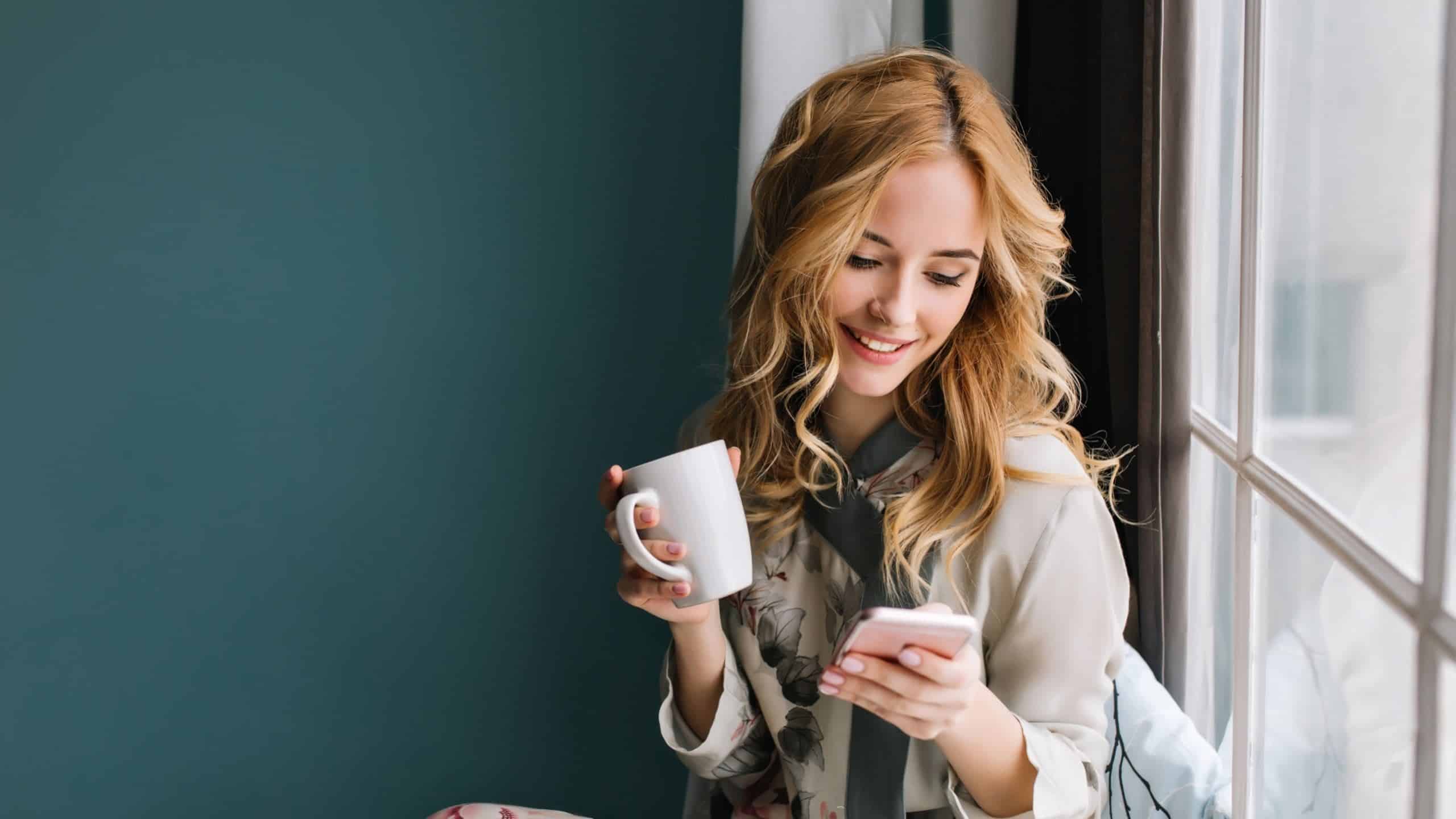 An attractive girl drinking coffee and texting on a mobile phone.