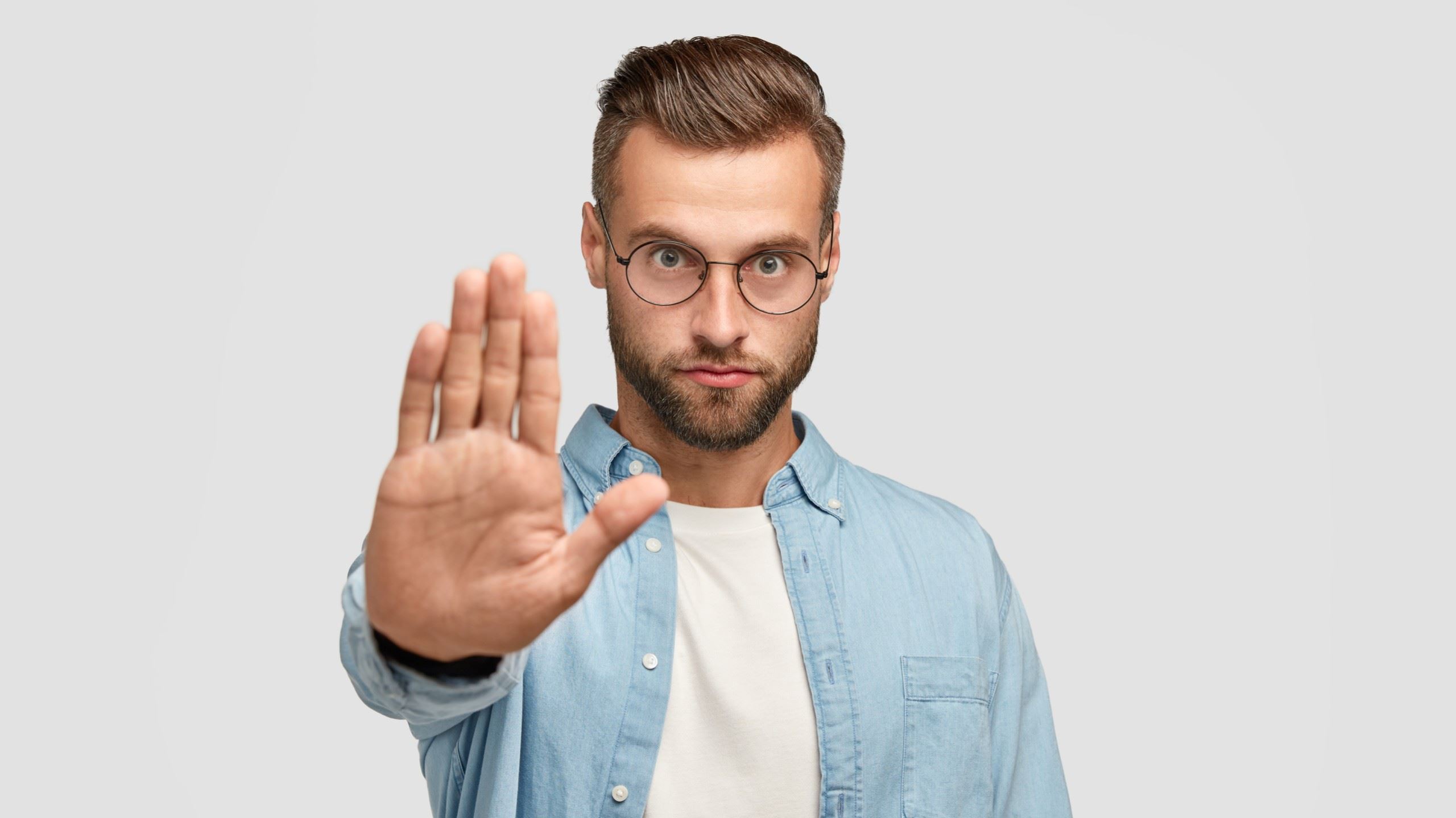 A man wearing glasses holding his hand in front of him and showing a stop-hand signal.