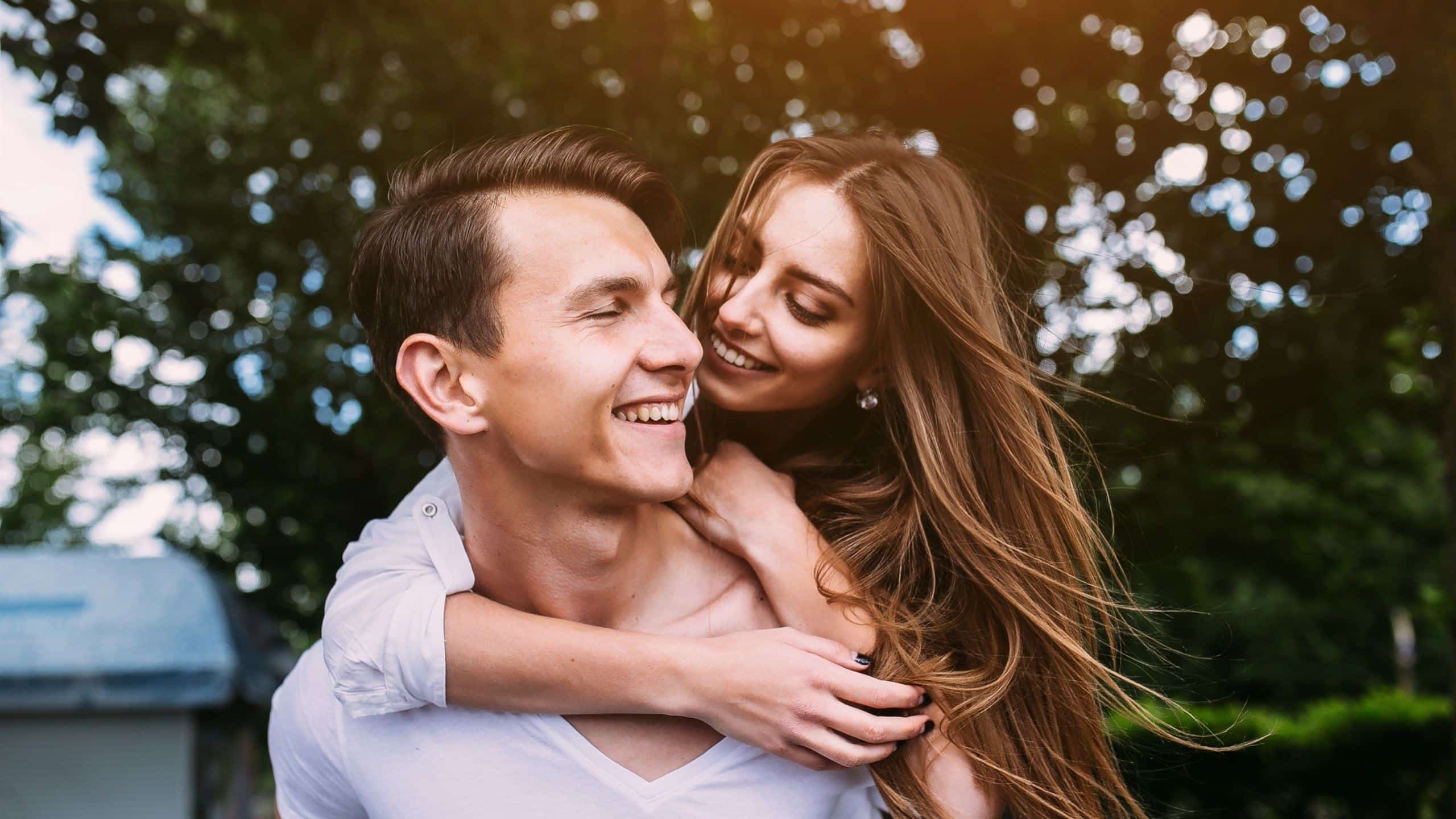 A man is carrying his girlfriend on his back while both look very happy.