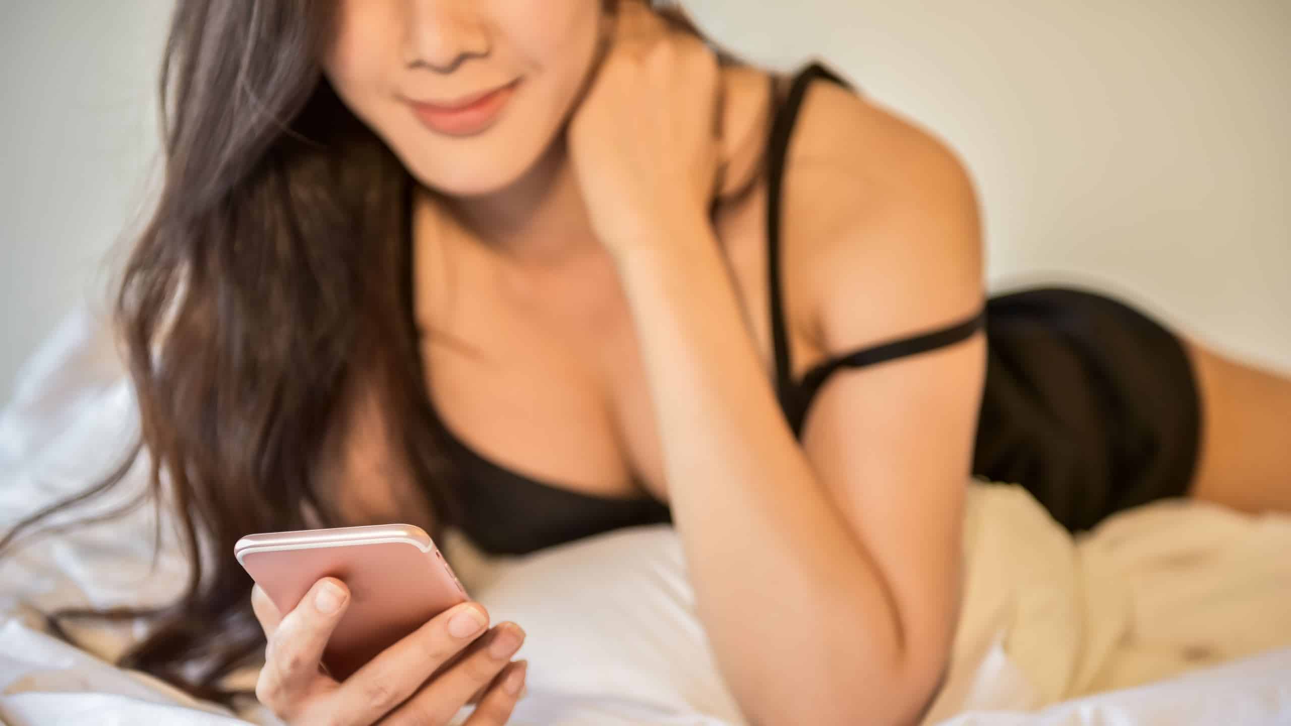 A woman in a bed reading a text message.