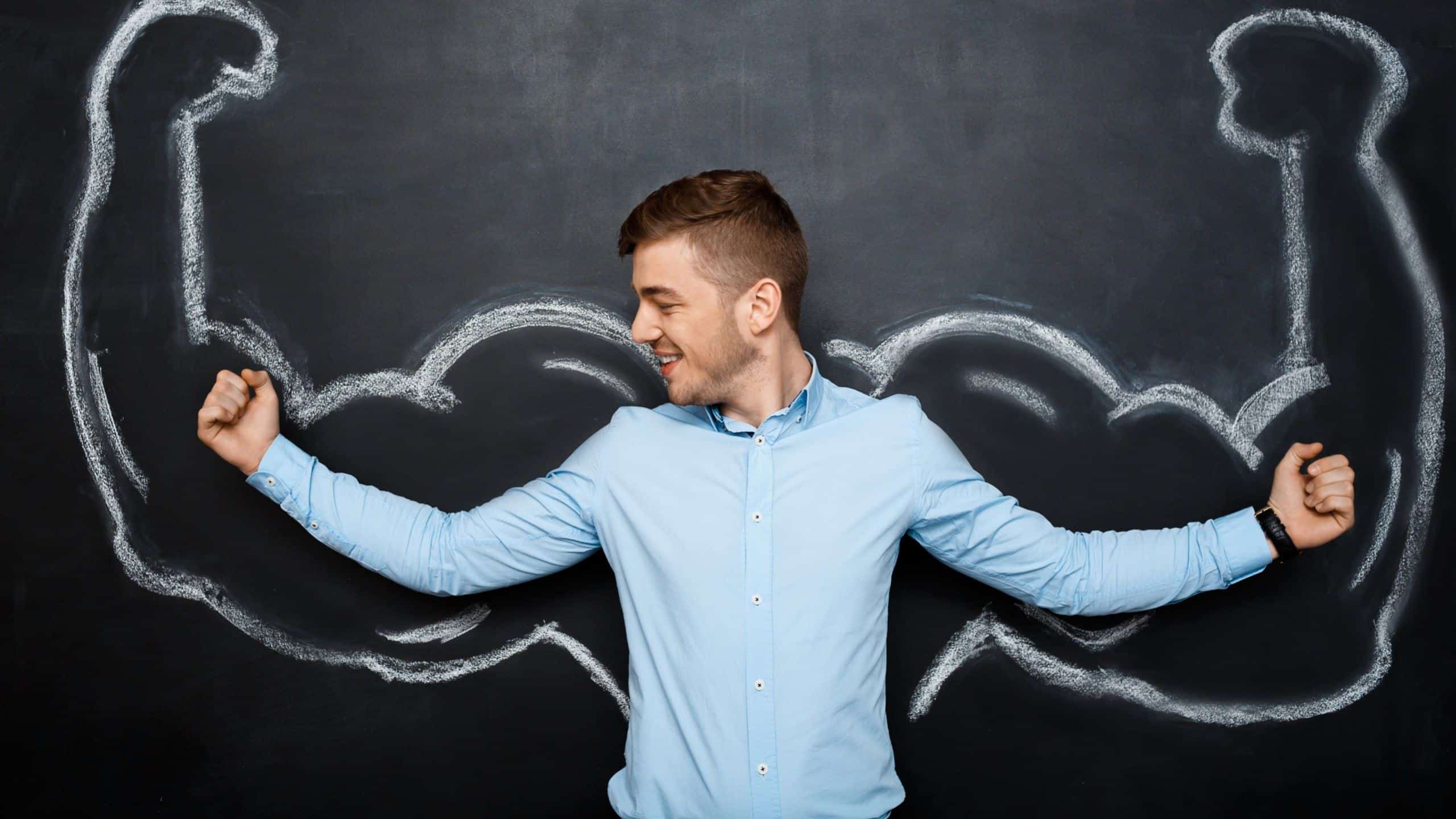 A man flexing his muscles in front of a chalkboard with drawn muscles.