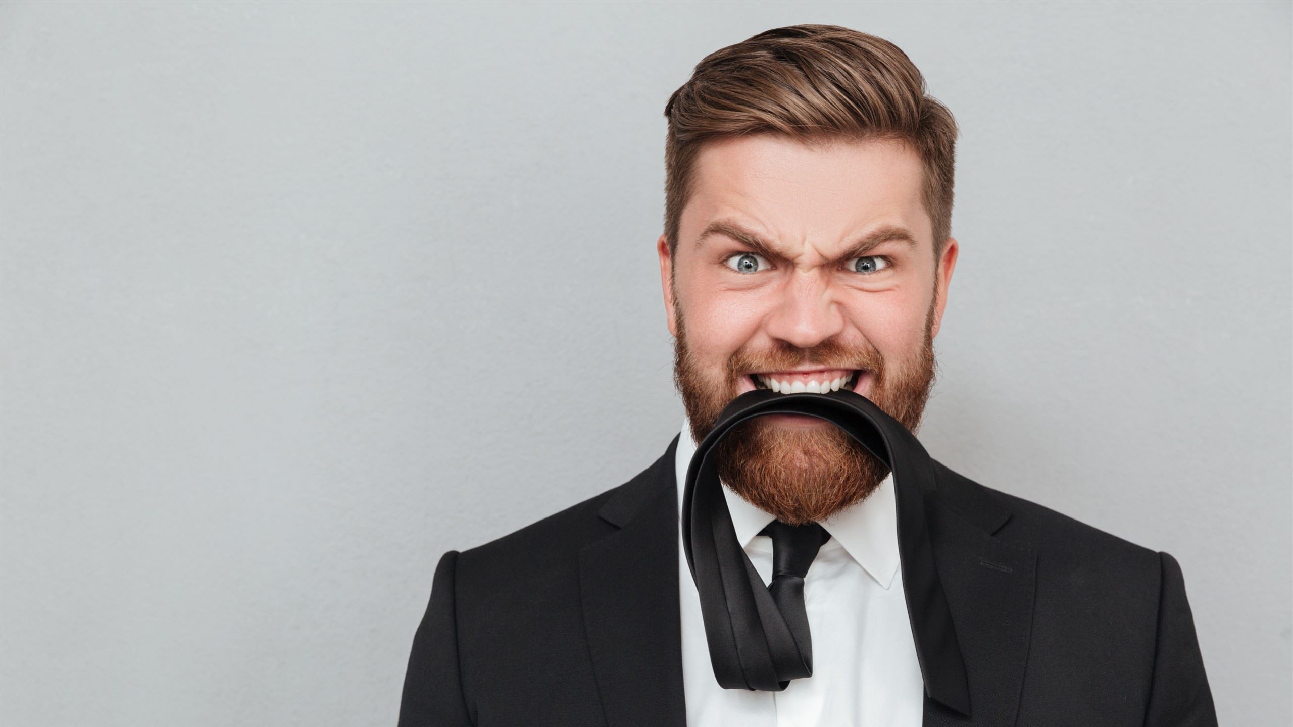 A wild guy holding his necktie between his teeth while making a crazy face.